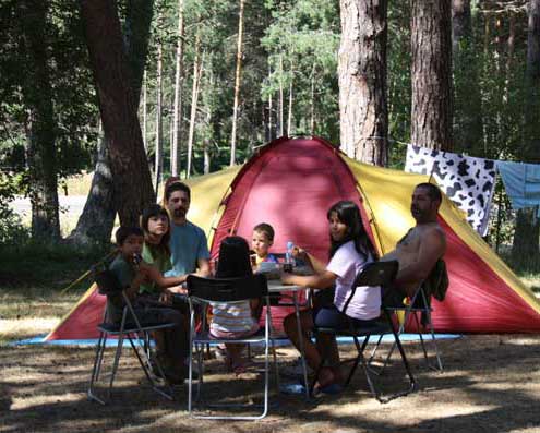 Campistas sentados alrededor de una mesa de camping, con una tienda al fondo